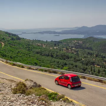 A small red car on the mountain road to the sea.
