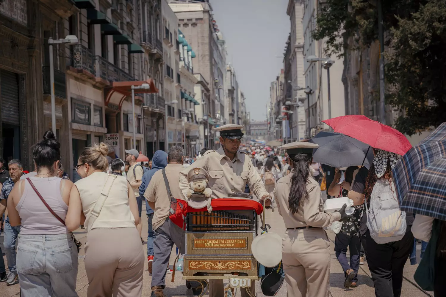 An organ grinder walks down a crowded pedestrian street in a city.