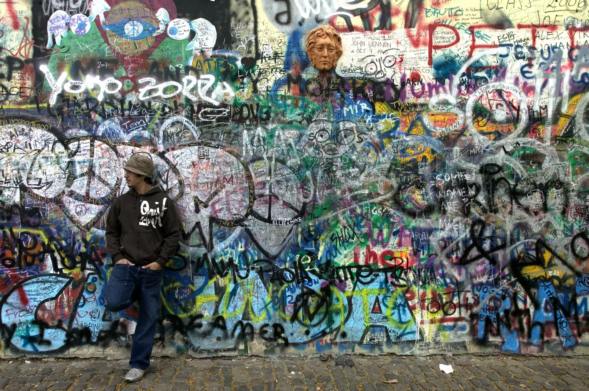 Man standing in front of graffiti, John Lennon Wall.