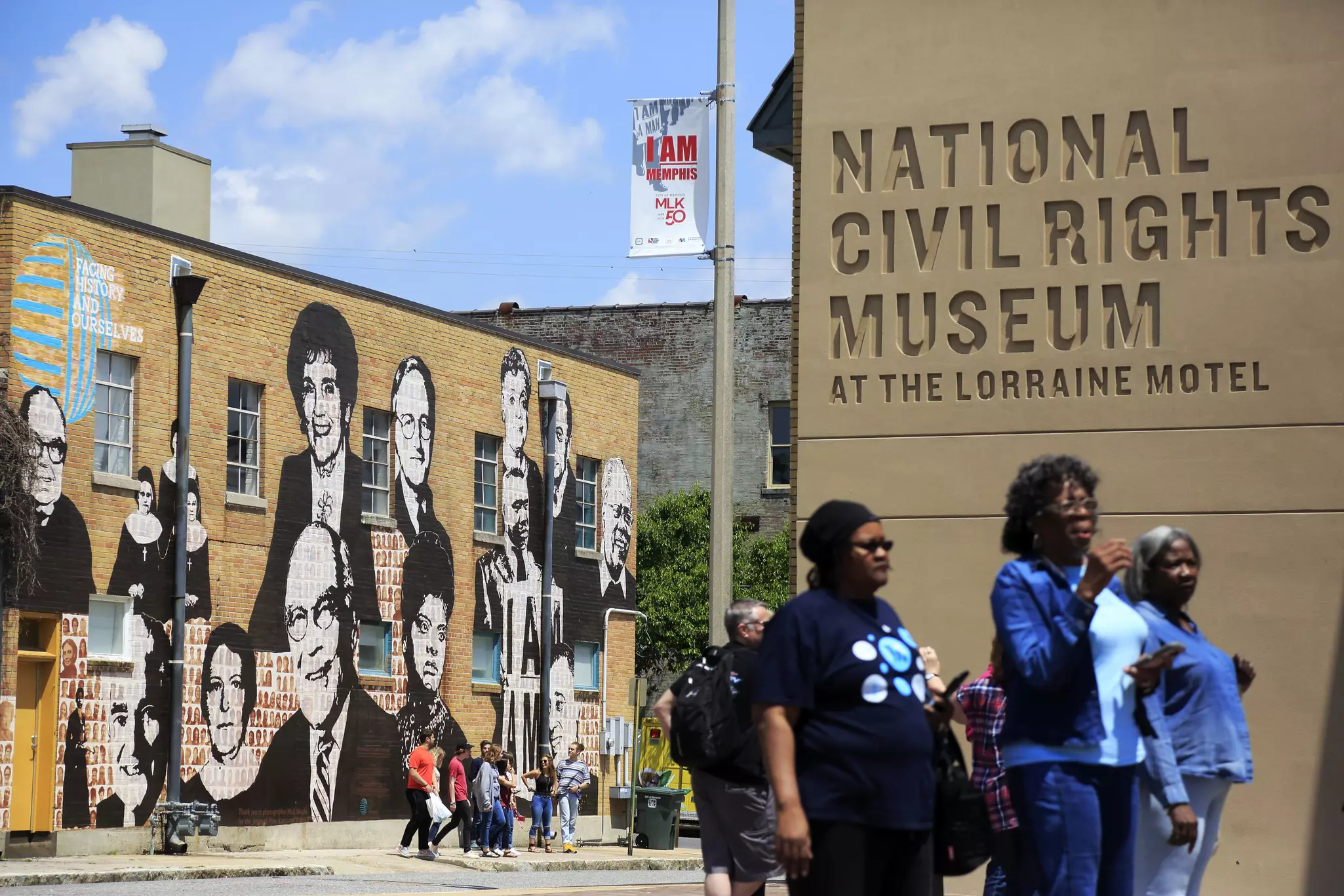Visitors outside of the National Civil Rights Museum in Memphis, Tennessee, USA. A mural depicting historic figures is seen on a wall in the background.