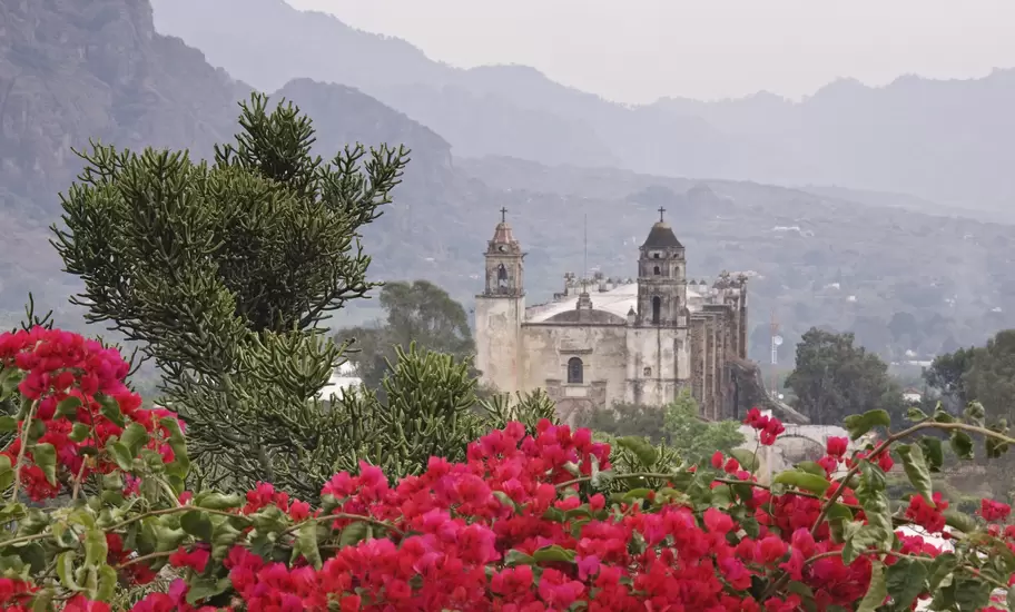 Twin-towered stone church of Tepoztlán's former convent below hazy mountains, pink bougainvillea in the foreground