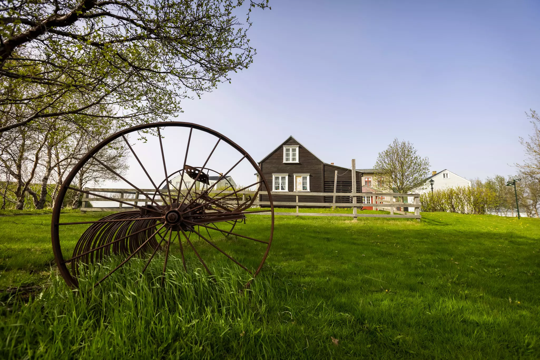 A rural landscape with an old plow and a low-rise house in the distance.
