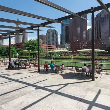 People sitting at tables under umbrellas at the Rose Kennedy Greenway's North End Park in Boston, Massachusetts.