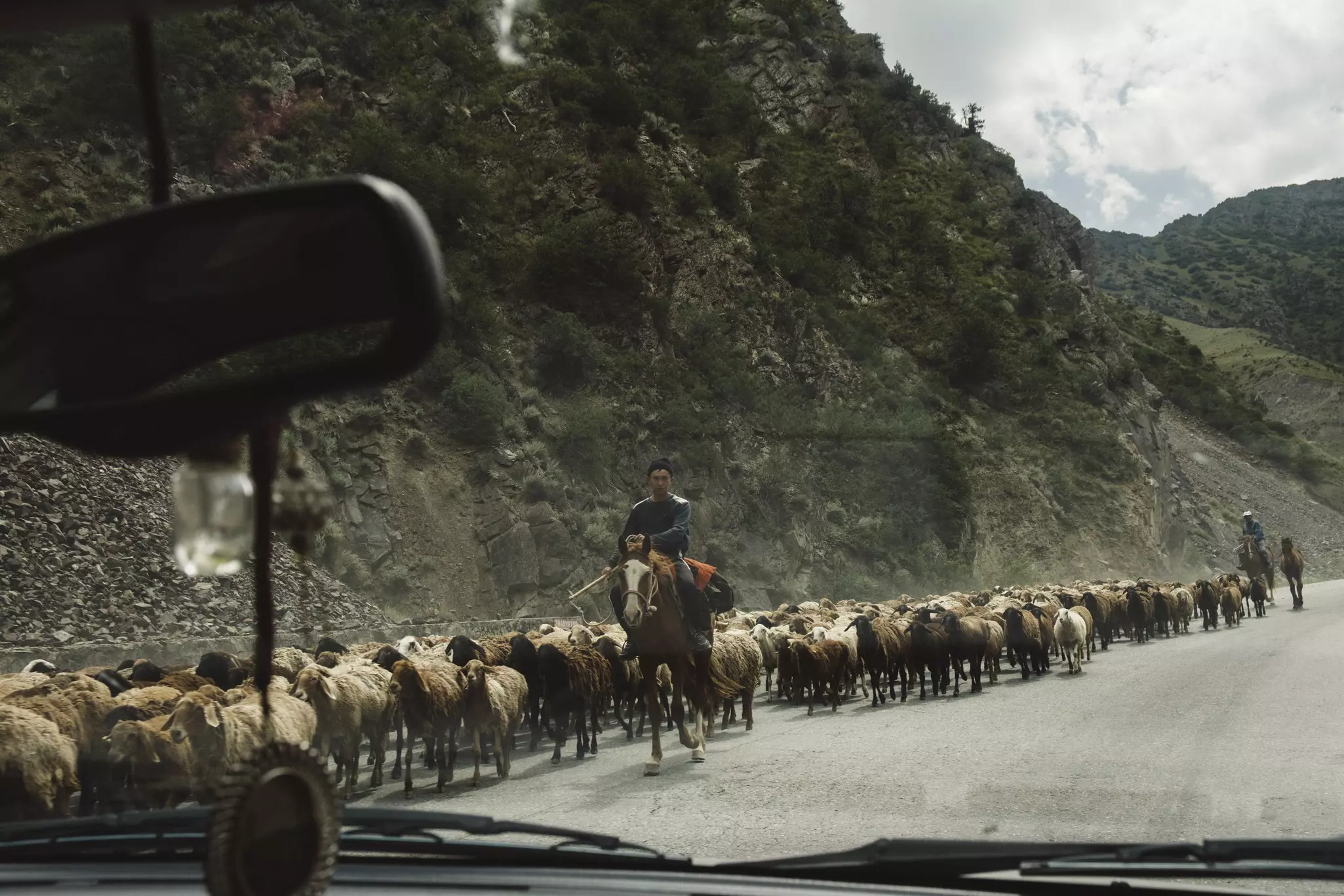 A man on horseback shepherding a flock of sheep on a main road in Kyrgyzstan.