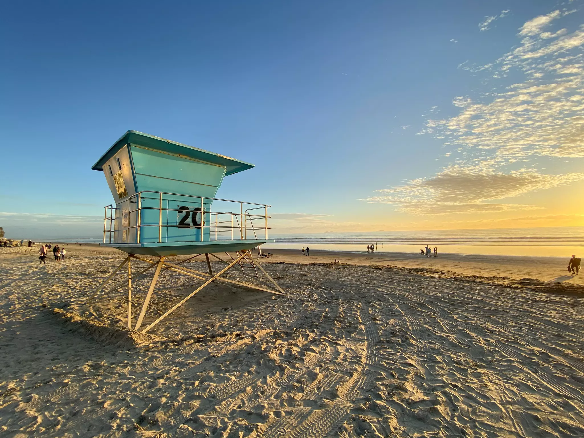 A wooden lifeguard lookout point on a sandy beach. People enjoy the sunset.