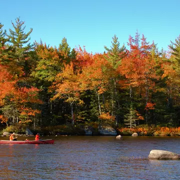 Two people paddle in a canoe through fall foliage at Kejimkujik National Park, Nova Scotia, Canada