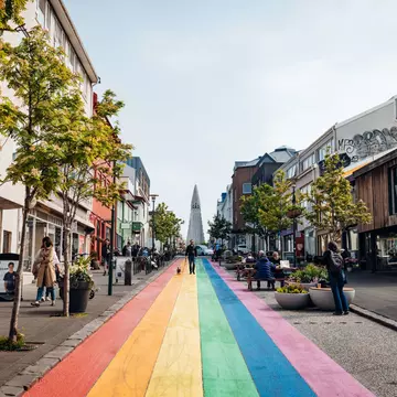 A street, with a walkway of striped rainbow colors, leads to the pointed spire of a cathedral in Reykjavik, Iceland.