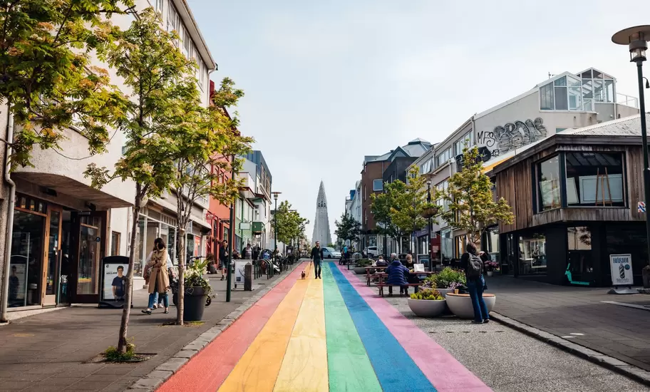A street, with a walkway of striped rainbow colors, leads to the pointed spire of a cathedral in Reykjavik, Iceland.