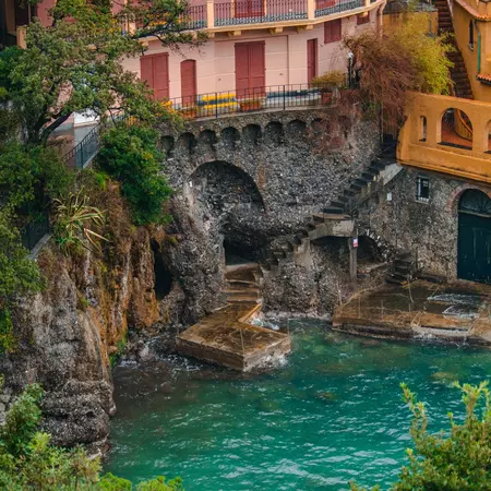 A pink building built on a high cliff with a stone dock and stairs built into the cliffside.