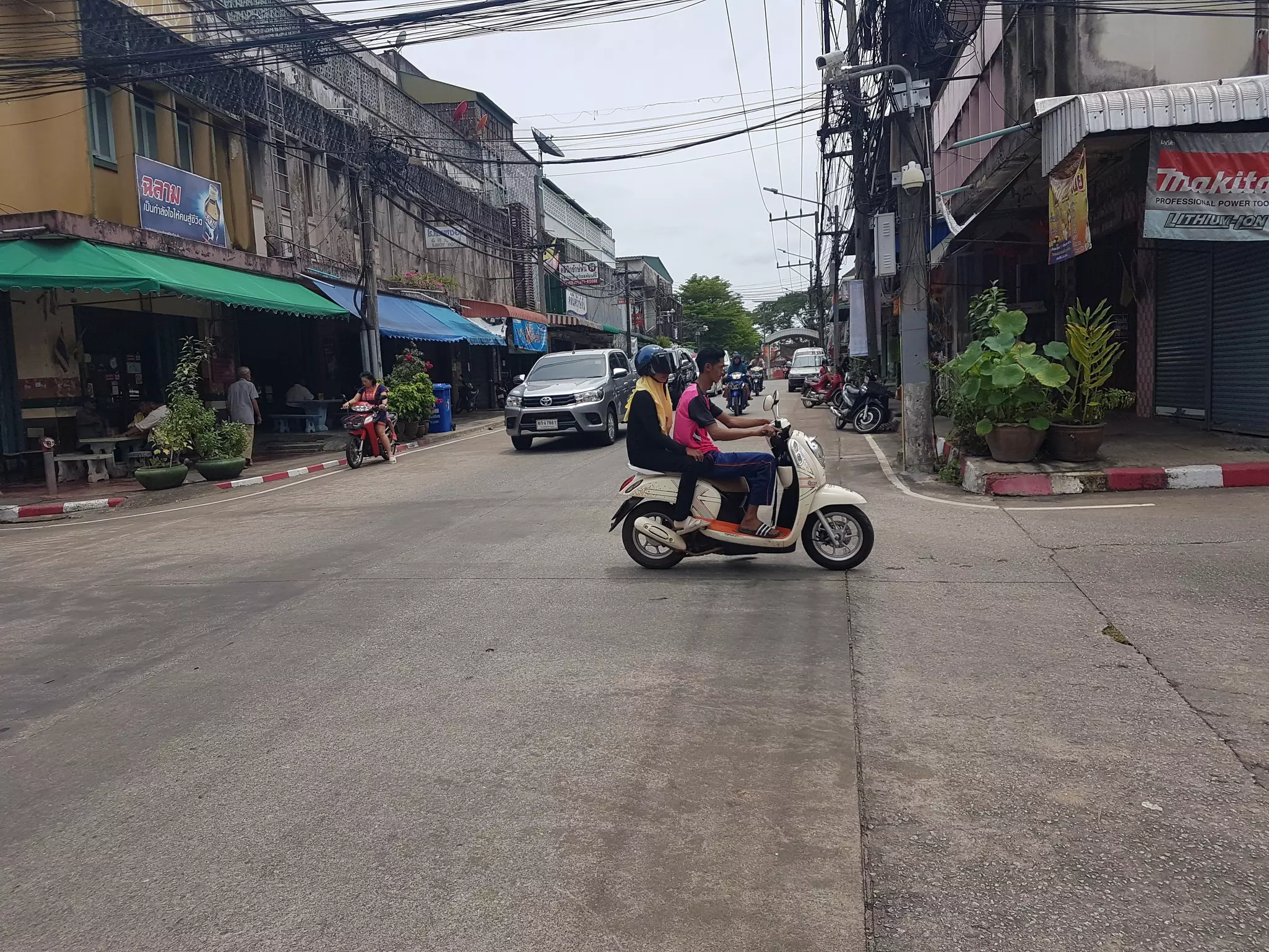 Two people on a scooter cross an intersection as cars approach