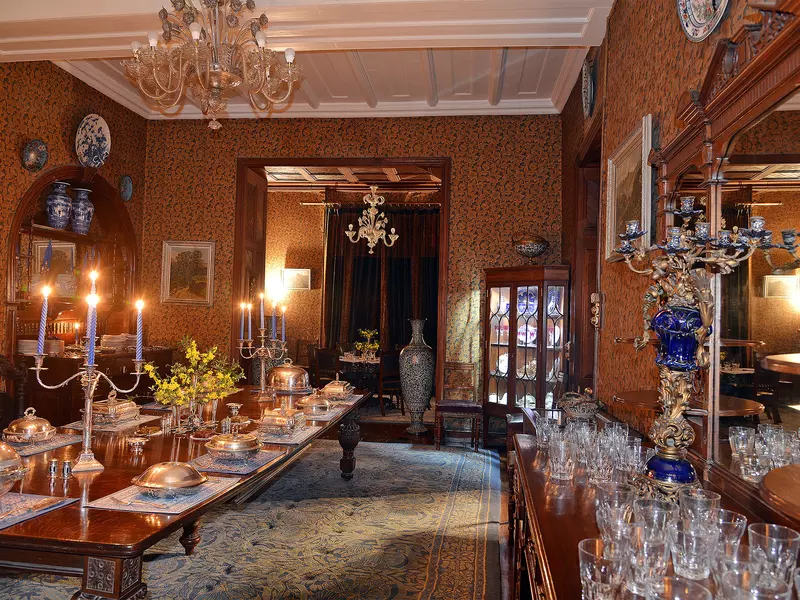 A large grand dining room with candles, ornate glasses and chandeliers.