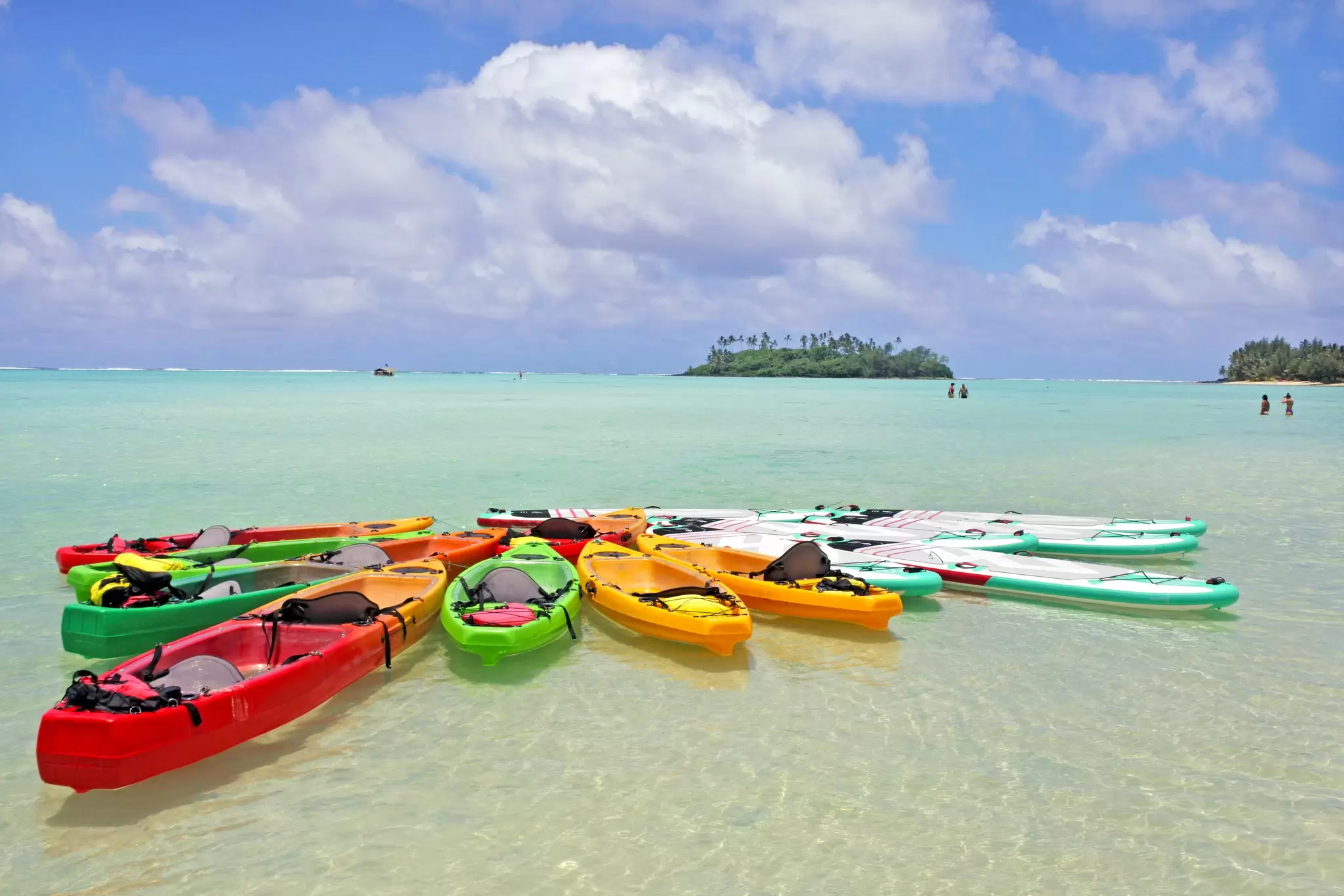 A group of kayaks and stand-up paddleboards moored together in the crystal-clear waters of a lagoon.