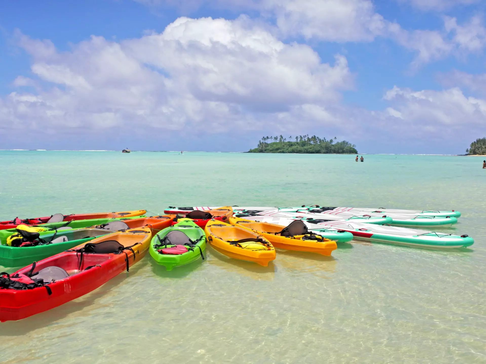A group of kayaks and stand-up paddleboards moored together in the crystal-clear waters of a lagoon.