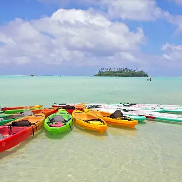 A group of kayaks and stand-up paddleboards moored together in the crystal-clear waters of a lagoon.