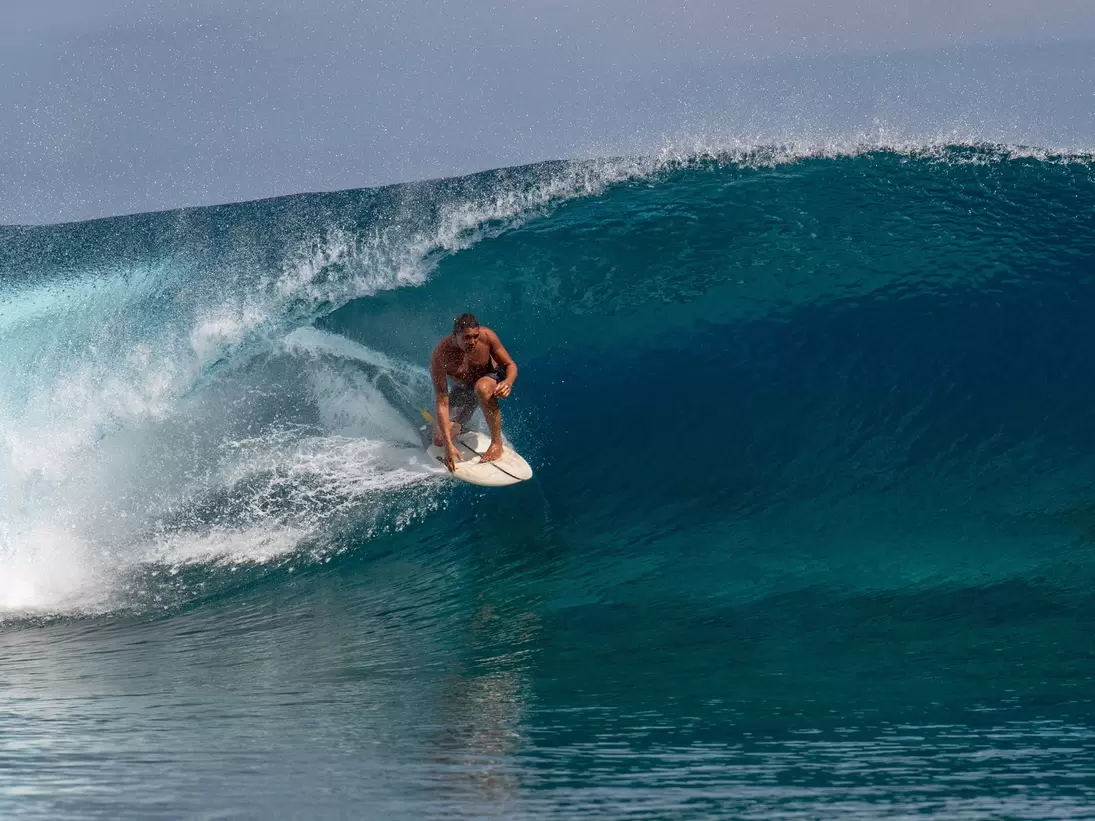 Surfer crouched on a board inside a large barreling wave at Teahupoʻo, Tahiti