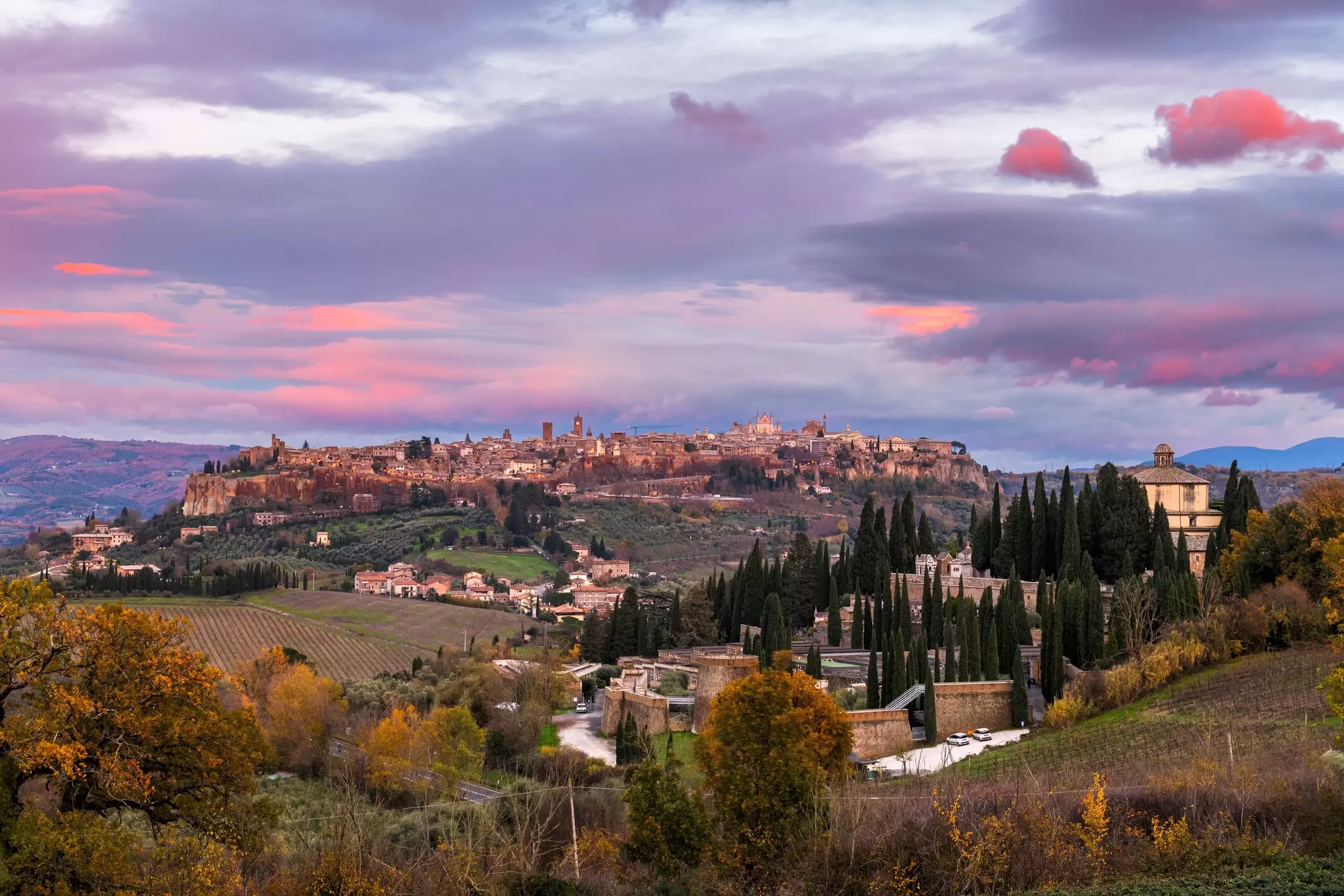 The Umbrian hill town of Orvieto, Italy, glowing under the fading light, surrounded by vineyards and trees in shades of gold during autumn
