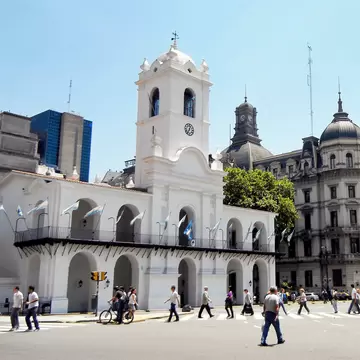Exterior of the historic Cabildo Nacional building in Plaza de Mayo, Buenos Aires. Pedestrians walking on busy street in foreground.