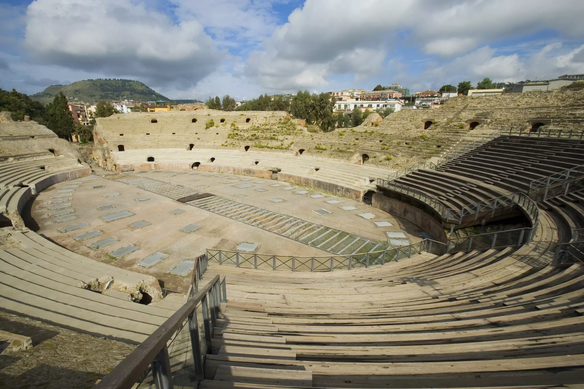 An overarching view of the Anfiteatro Flavio in Pozzuoli  with homes and clouds in the distance.