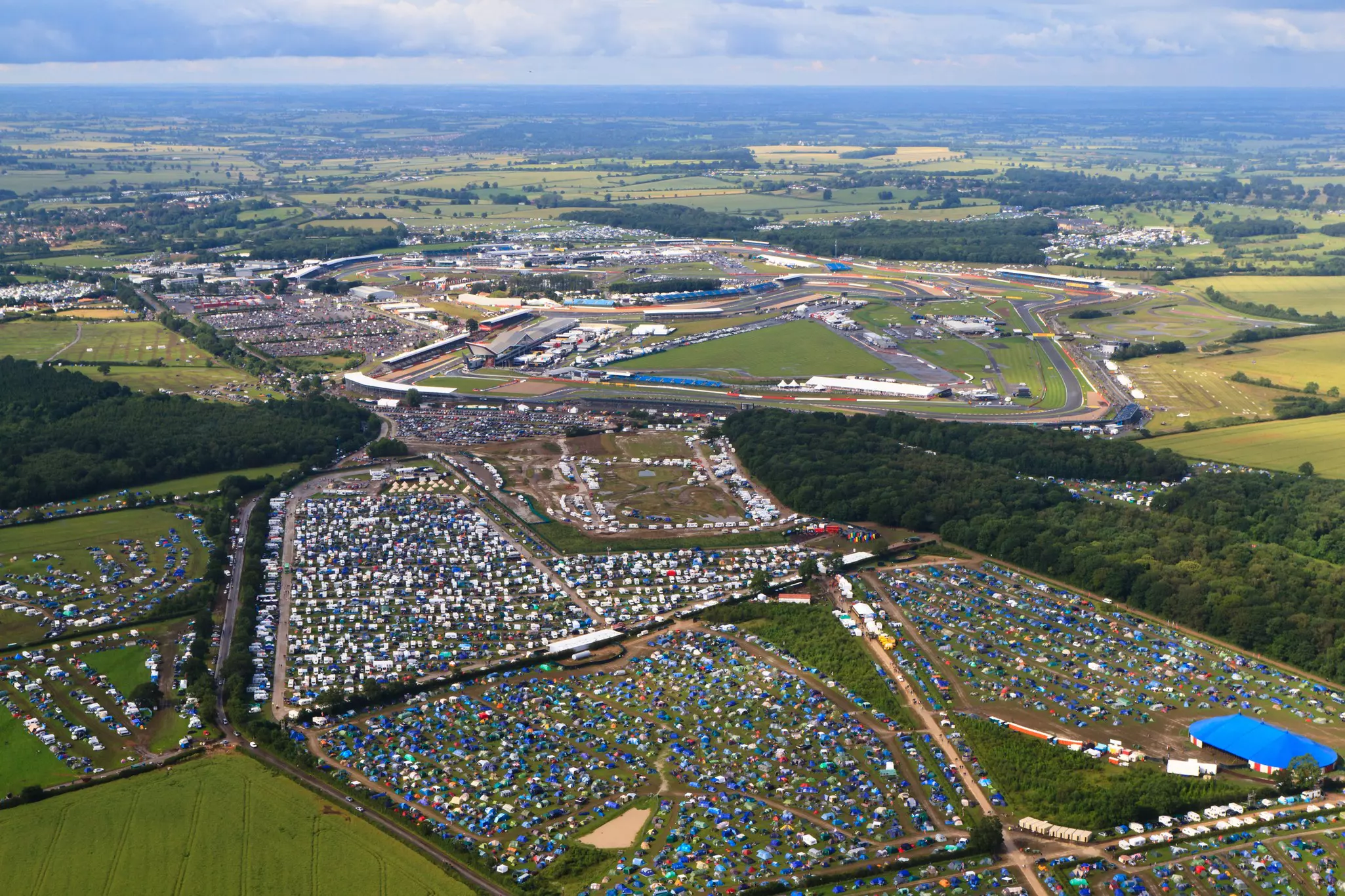 Many tents pitched in fields surrounding a race track