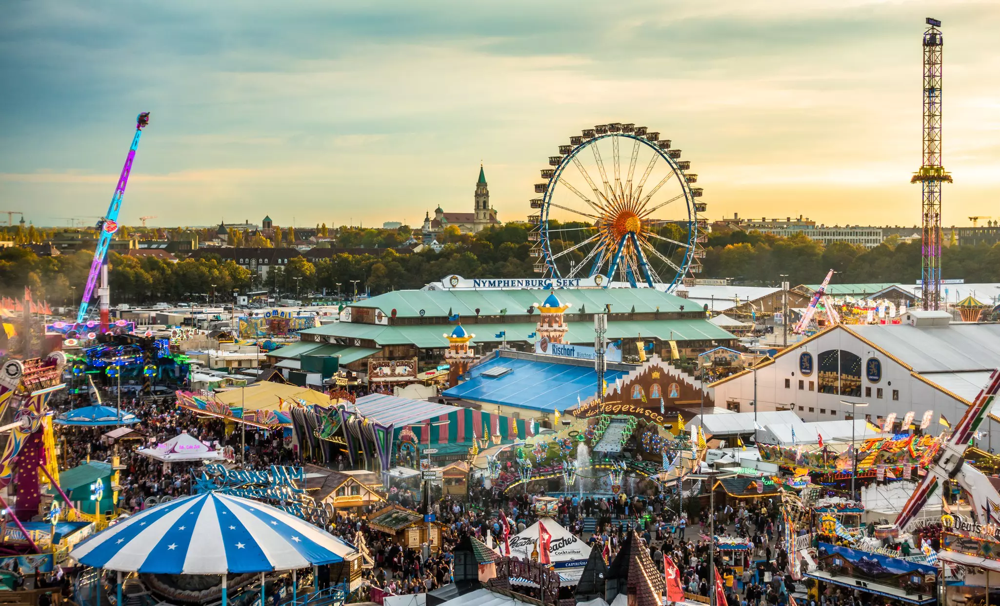 A fairground site with a Ferris wheel, rides and large tents.