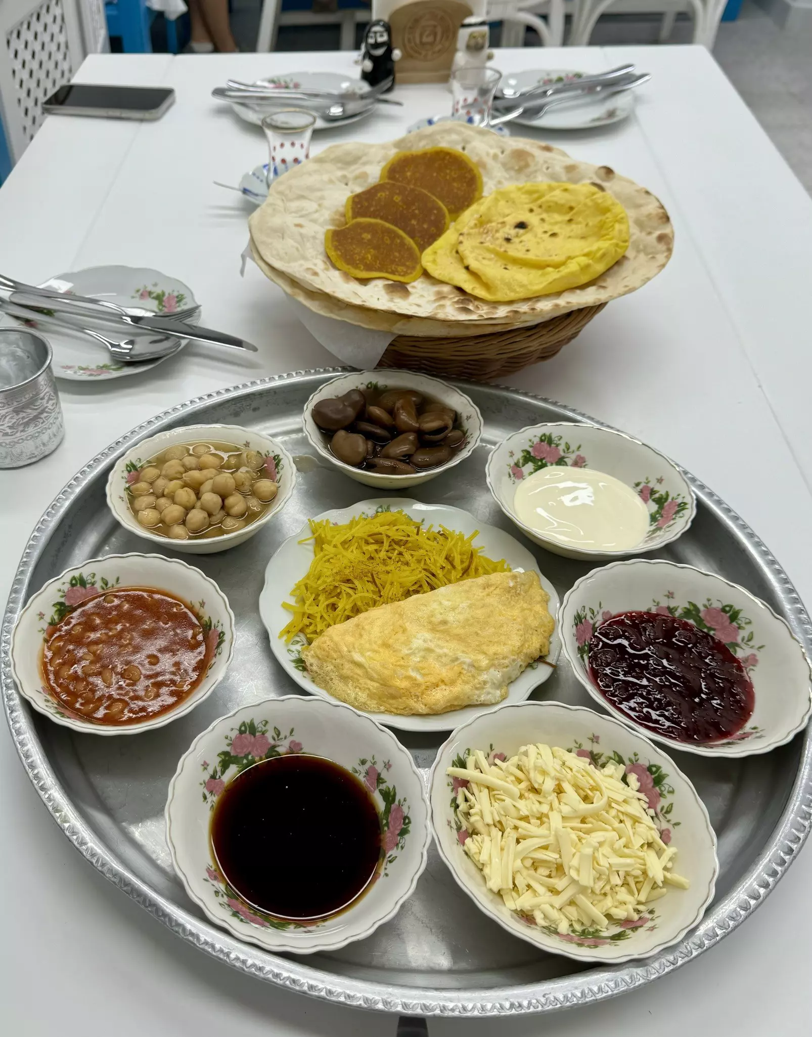 A silver platter topped with small dishes that include sliced cheese, beans, an omelette, chickpeas, sauces, olives and other traditional Emirati breakfast plates