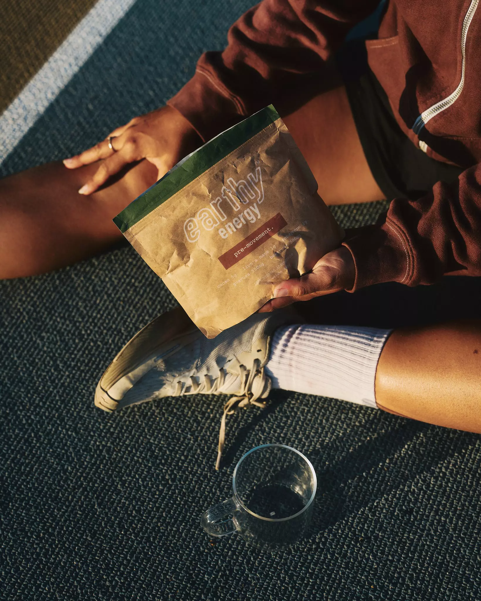 A person sitting on a rug holding a packet of Earthy; an empty glass mug is to the side.