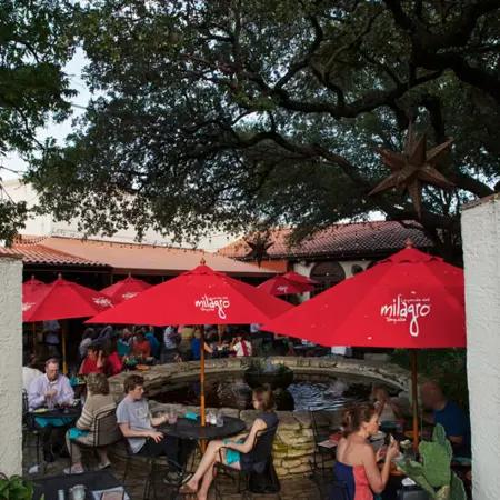 Red umbrellas above black tables filled with people surround a stone pool on the patio at Matt's El Rancho