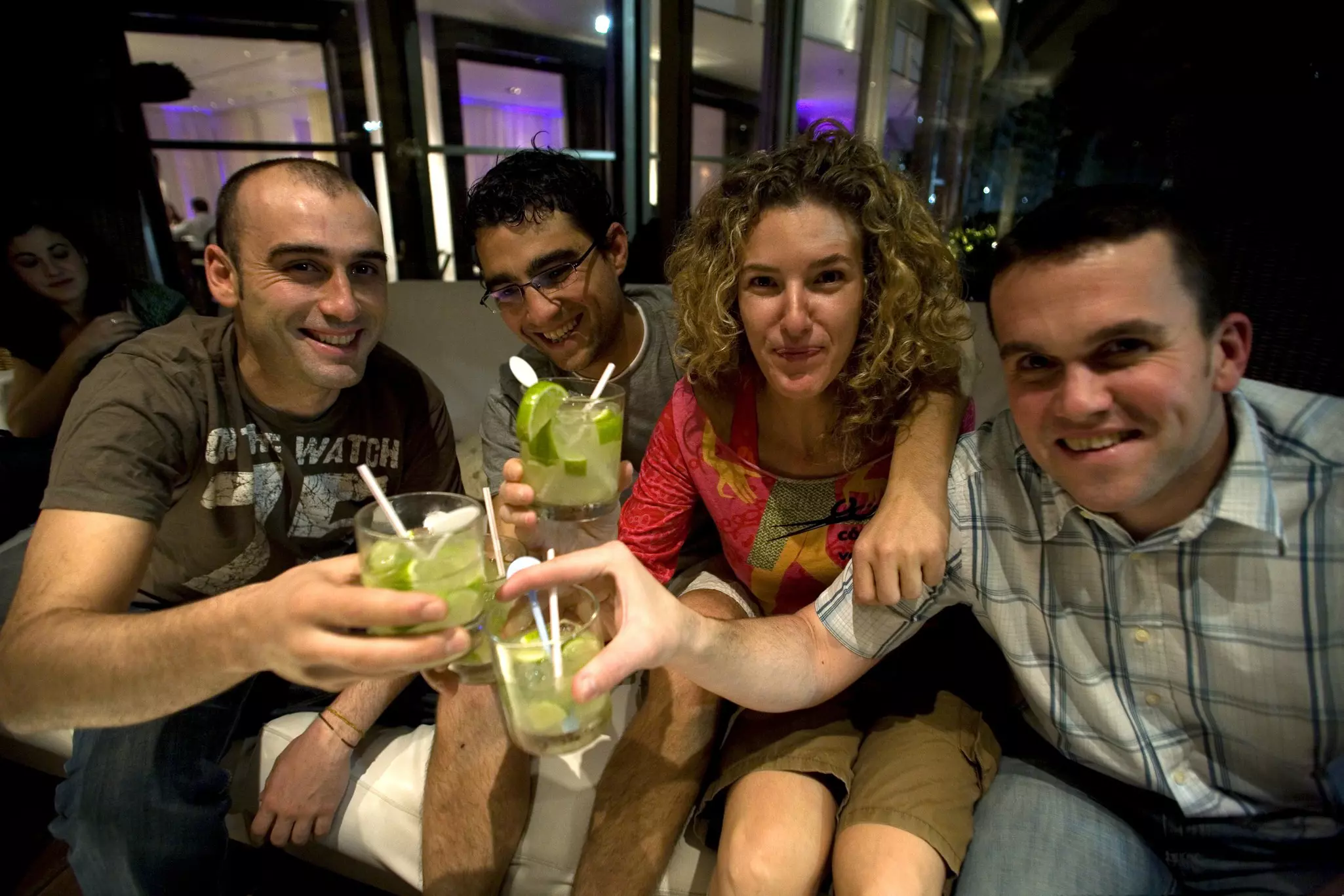 On the left, a man and woman drink caipirinhas from a plastic glass. On the right, a close up of a caipirinha at sunset with the beach and sea in the background
