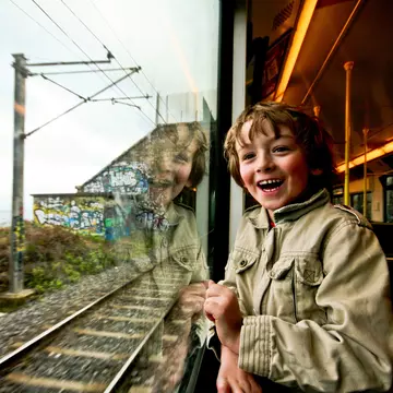 A very excited young boy looks out of a train window.