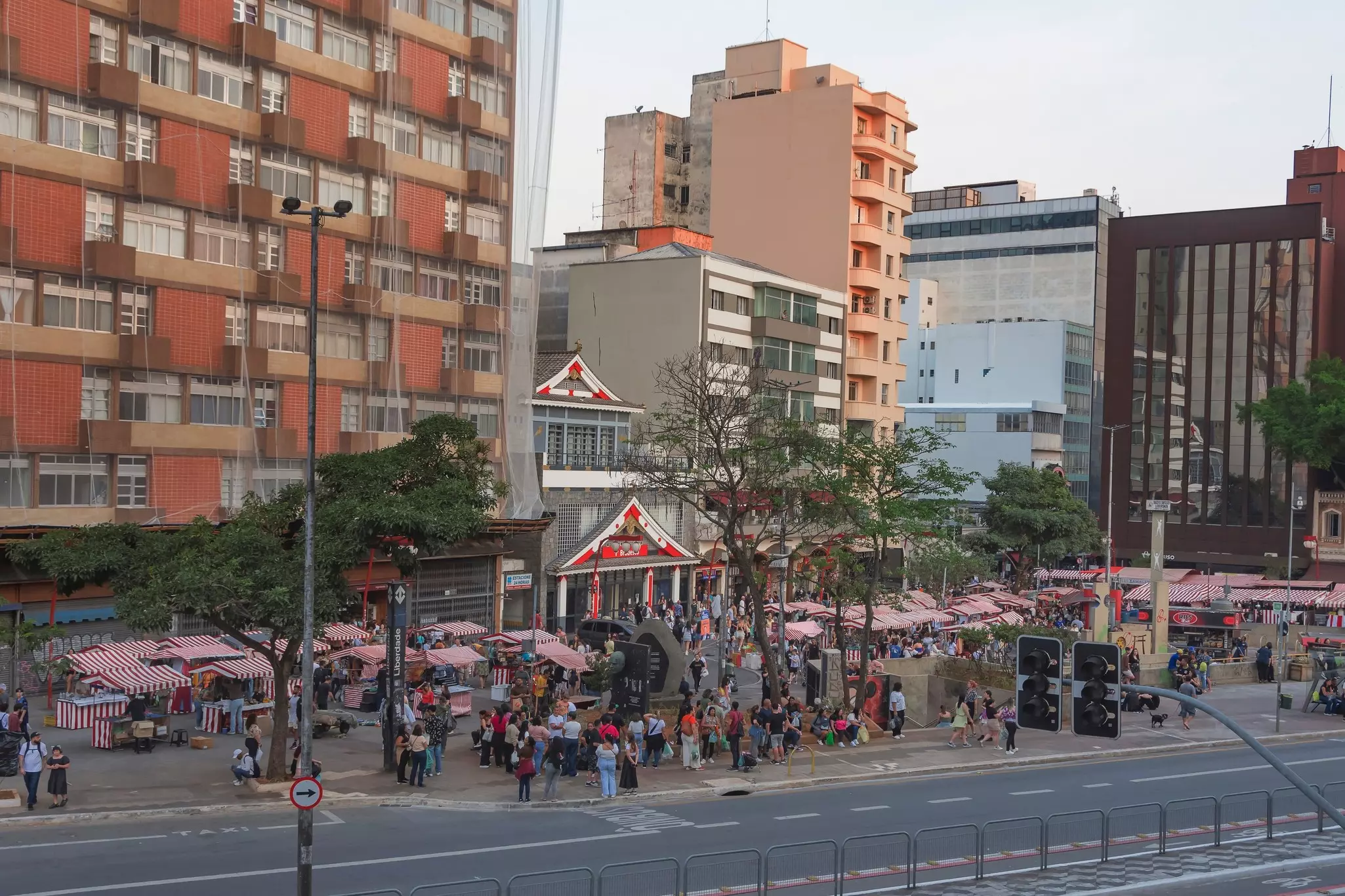 A series of market stalls with red and white canopies line a sidewalk in a city neighborhood.
