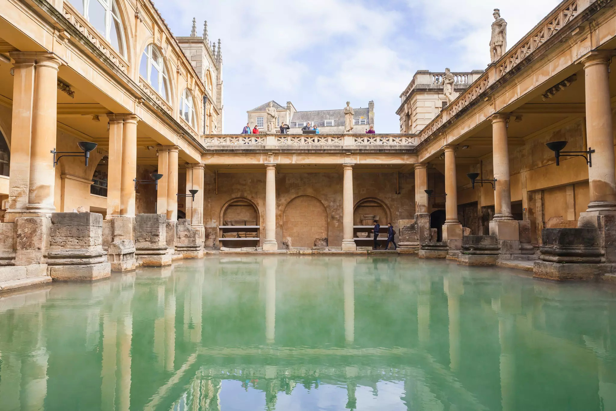 A rectangular Roman bath with steam rising out of the water on an overcast day.