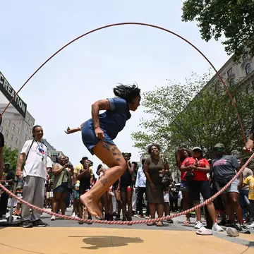 A woman jumps double dutch as a small group gathers around during a Juneteenth event along Black Lives Matter Plaza in Washington, DC