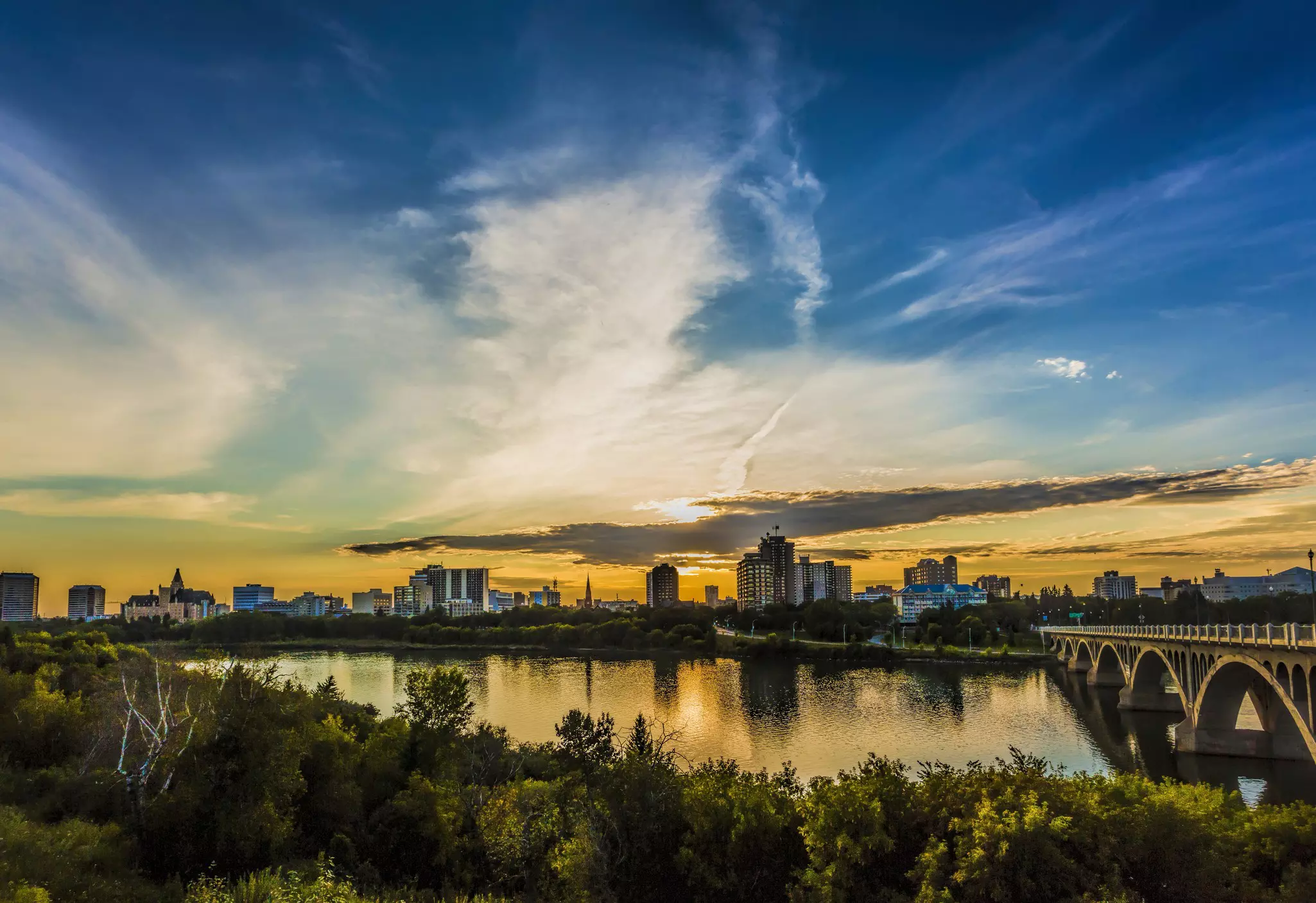 The skyline of a small city beside a river at sunset.