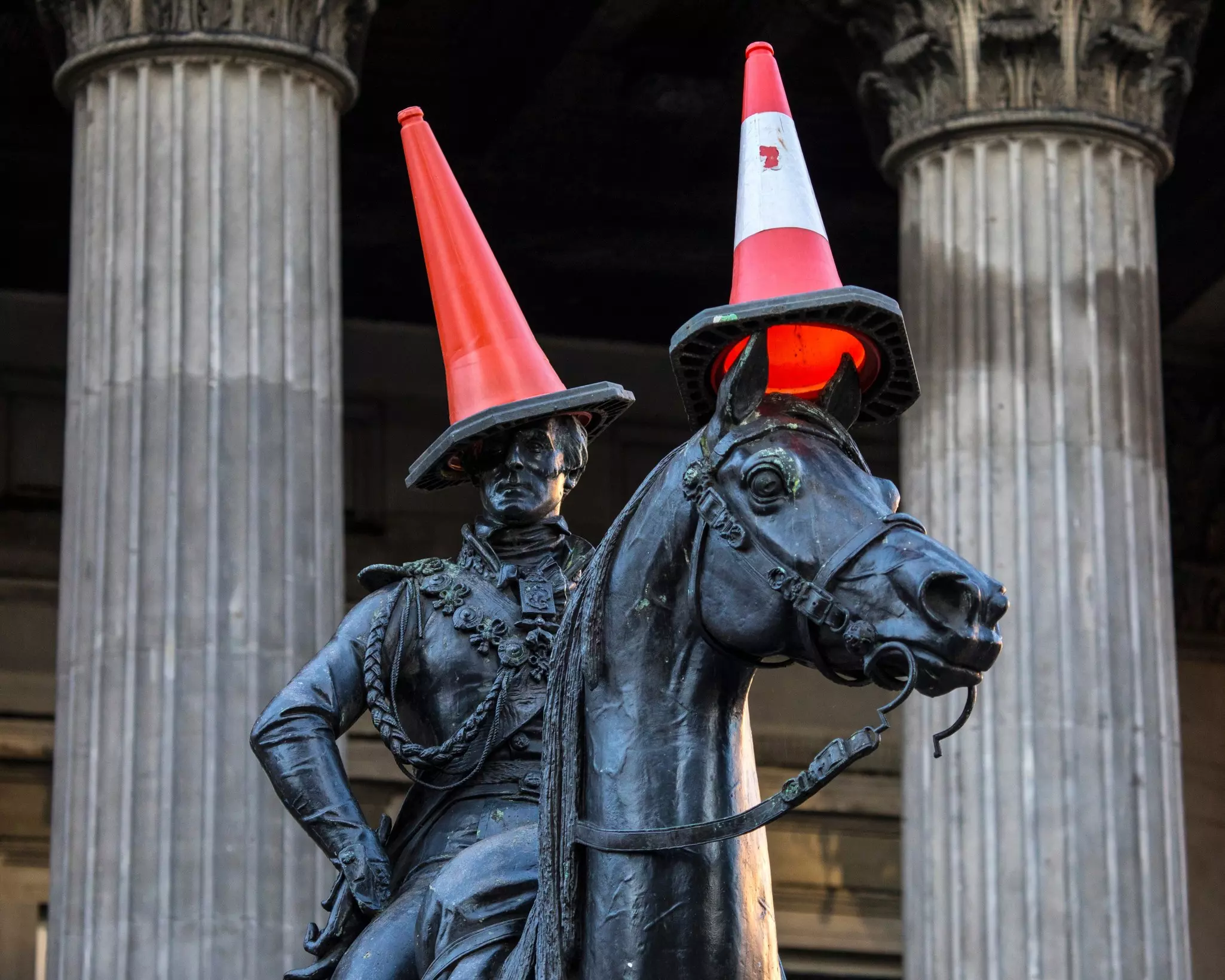 A statue of a man on a horse in central Glasgow, Scotland; orange traffic cones have been placed on the heads of the man and the horse.