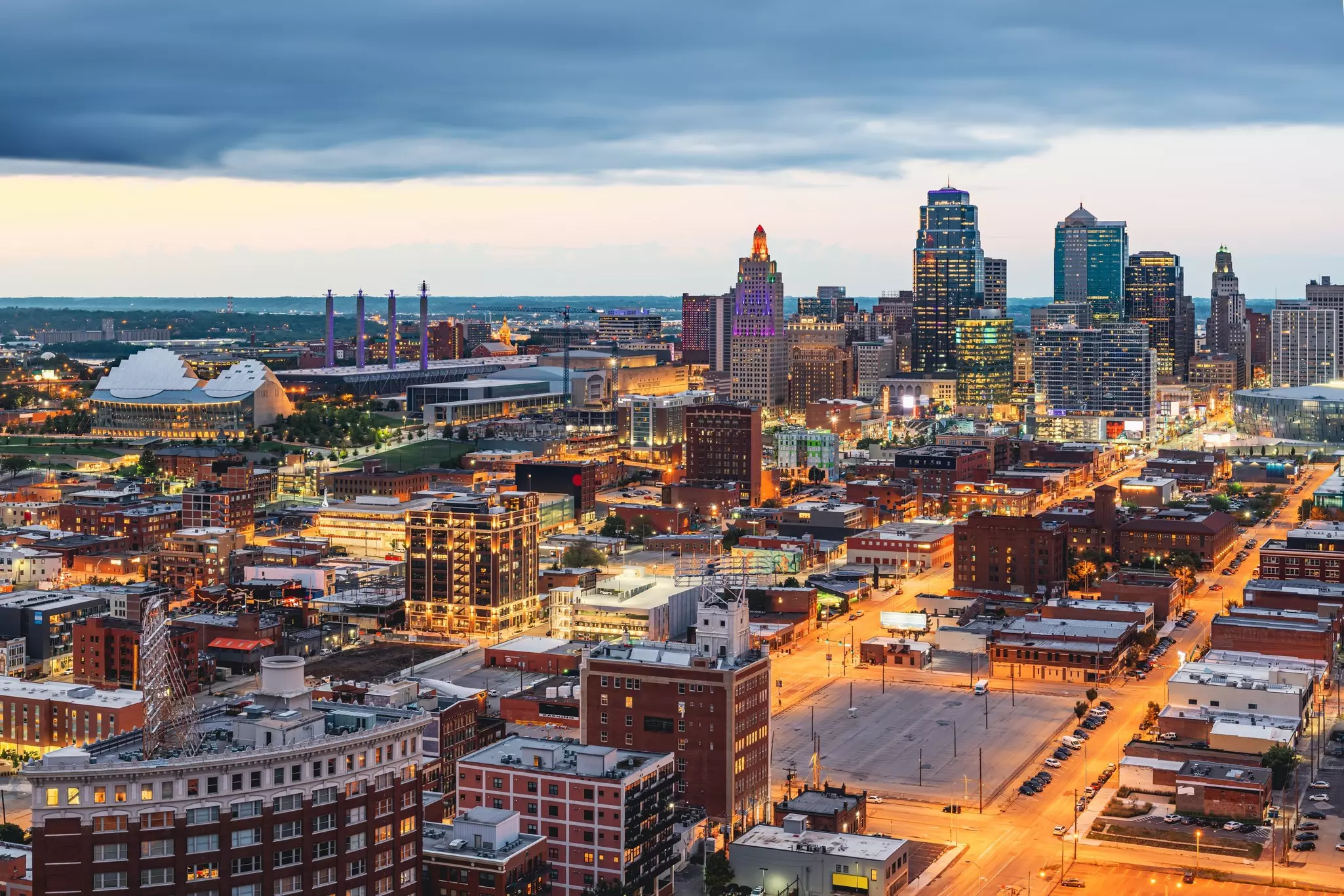 An aerial view of a city in the evening, with office towers and illuminated streets.