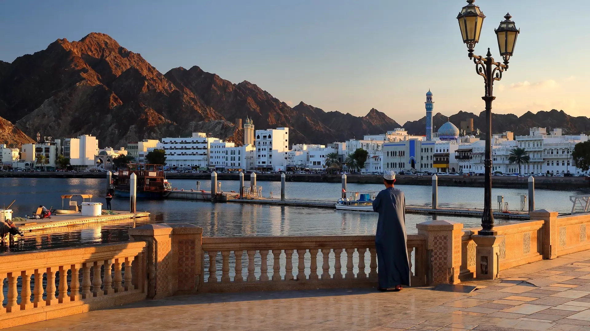 The Muttrah corniche viewed from the esplanade next to the fish market at sunset, with an Omani man traditionally dressed and the mosque and mountains in the background, Muttrah, Muscat, Oman