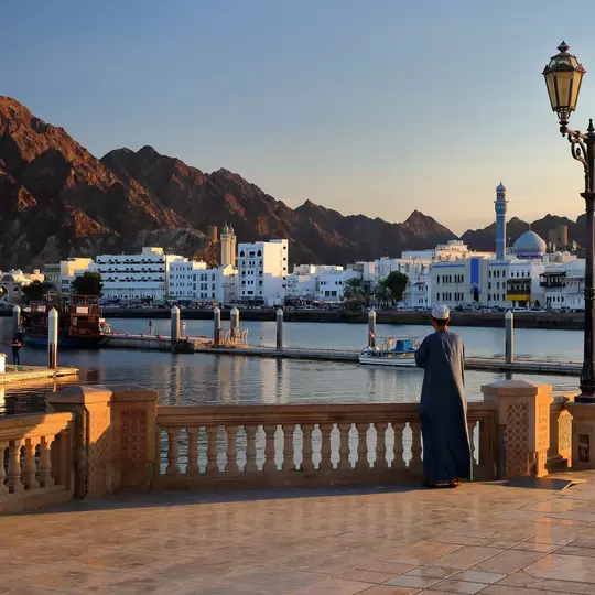 The Muttrah corniche viewed from the esplanade next to the fish market at sunset, with an Omani man traditionally dressed and the mosque and mountains in the background, Muttrah, Muscat, Oman