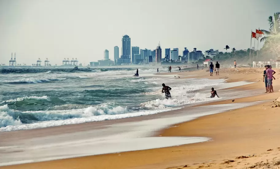 Swimmers in the surf at Mount Lavinia Beach with the high-rise skyline and port cranes of Colombo, Sri Lanka, behind