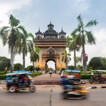 Tuk-tuks pass the Patuxai monument in central Vientiane, Laos. Jon Chica/Shutterstock
