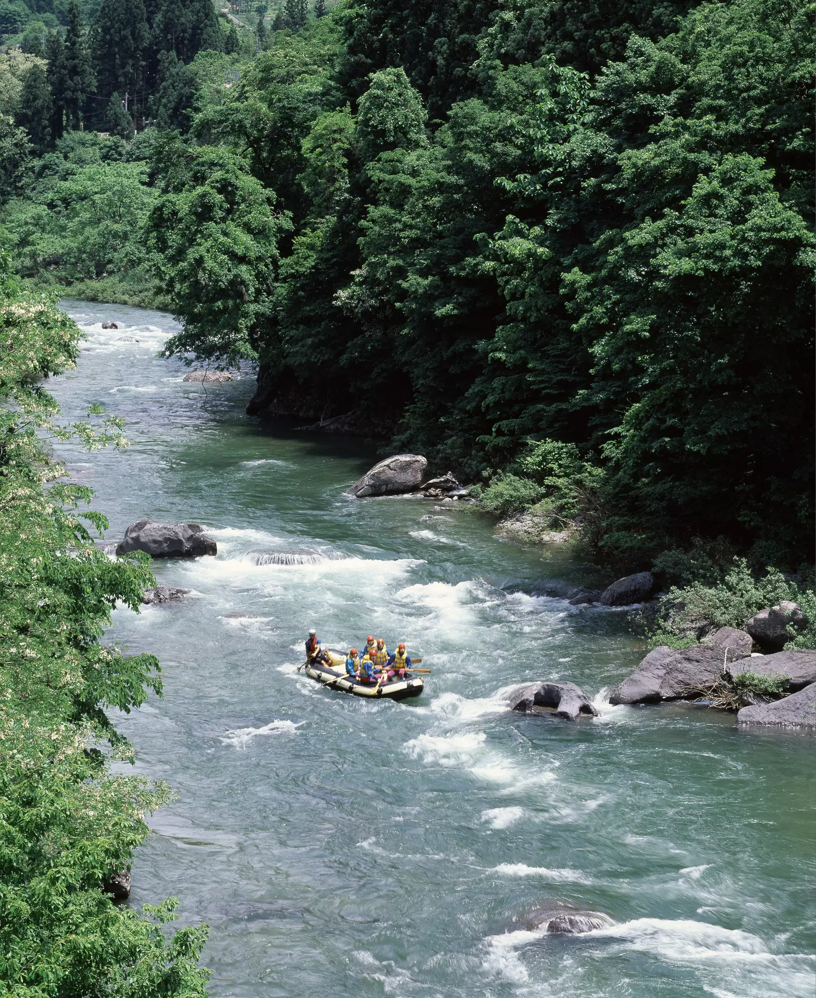 Looking down from above at a group of paddlers riding a raft through a raging river canyon