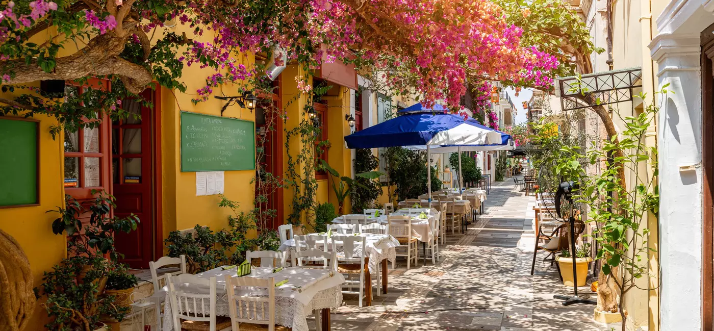 A narrow street lined with restaurants and shaded by trees in full bloom