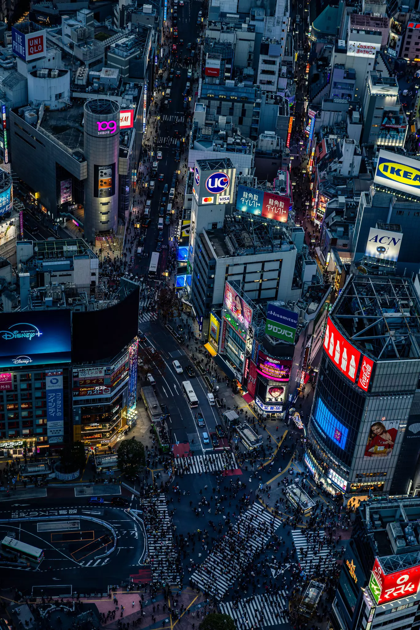 A viewing deck in a tall building looking down over a high-rise city where people are crossing the roads of a busy intersection.