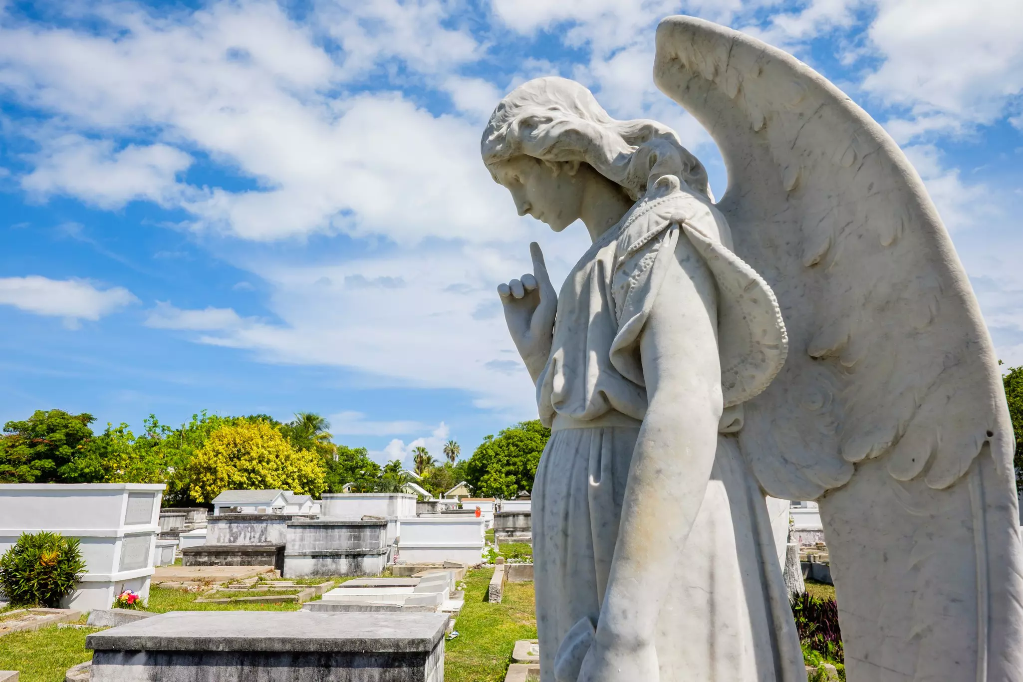 A stone sculpture of a winged angel is in a cemetery with mausoleums.