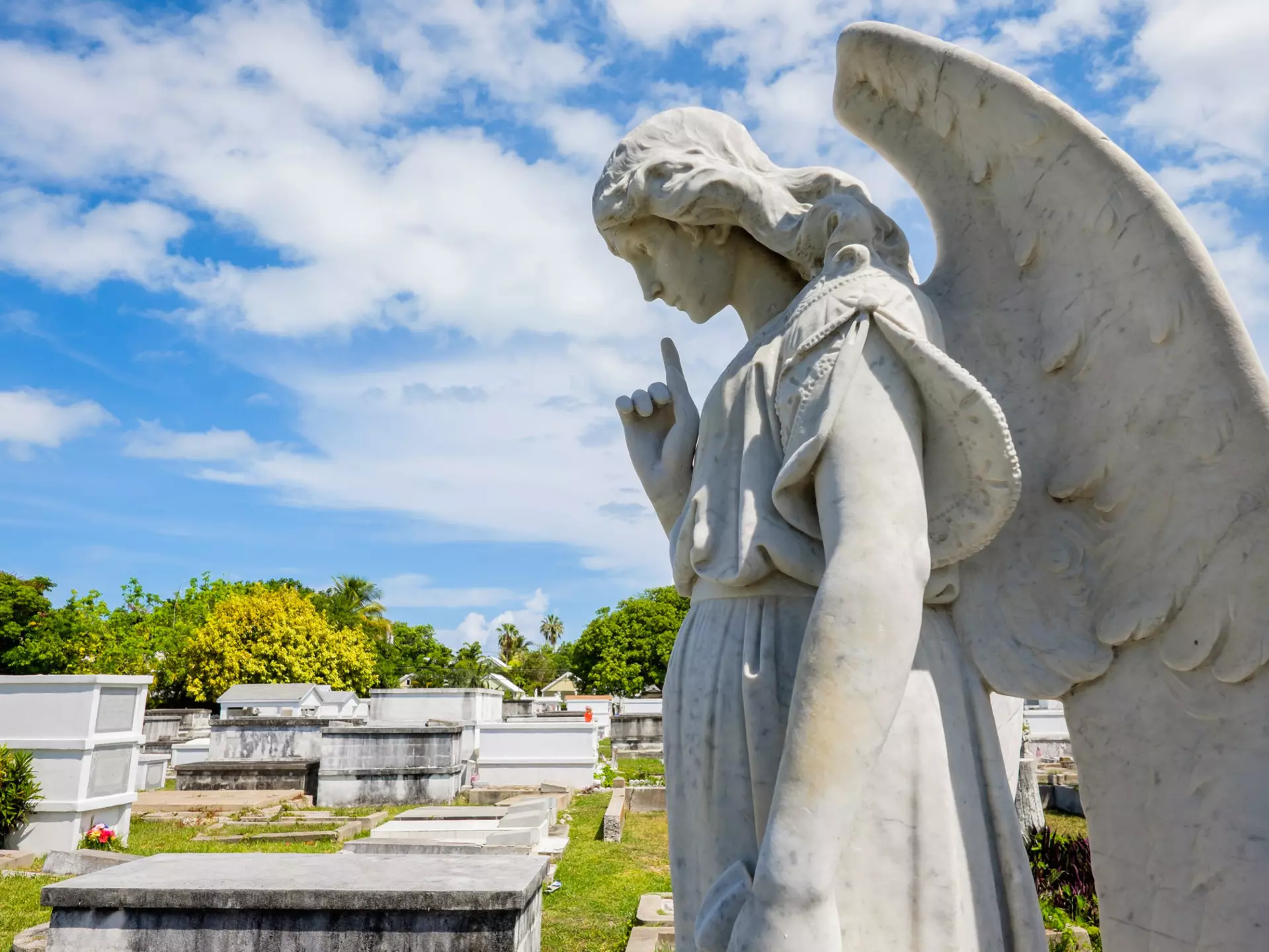 A stone sculpture of a winged angel is in a cemetery with mausoleums.