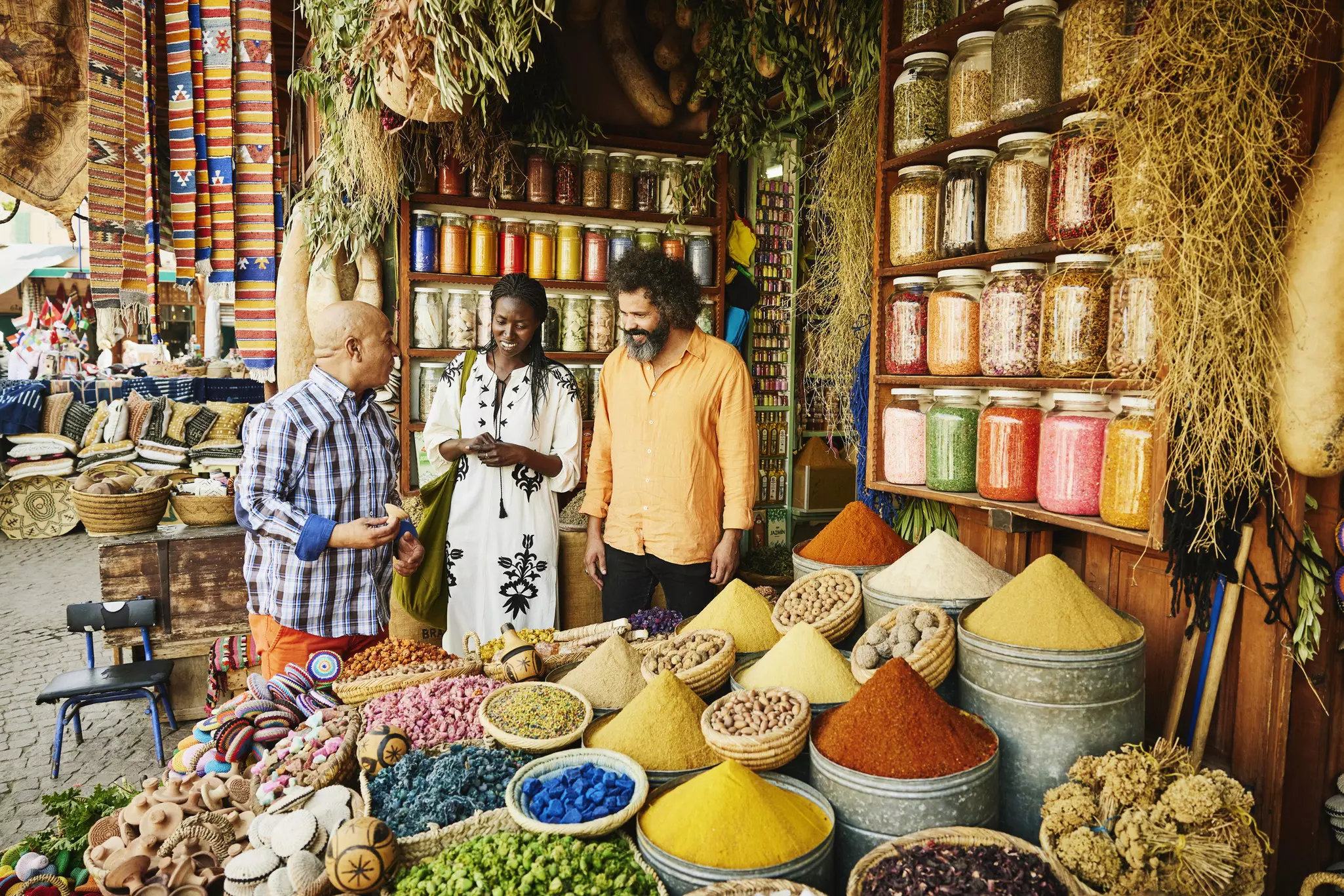 A couple talks to spice shop owner next to piles of colored spices.