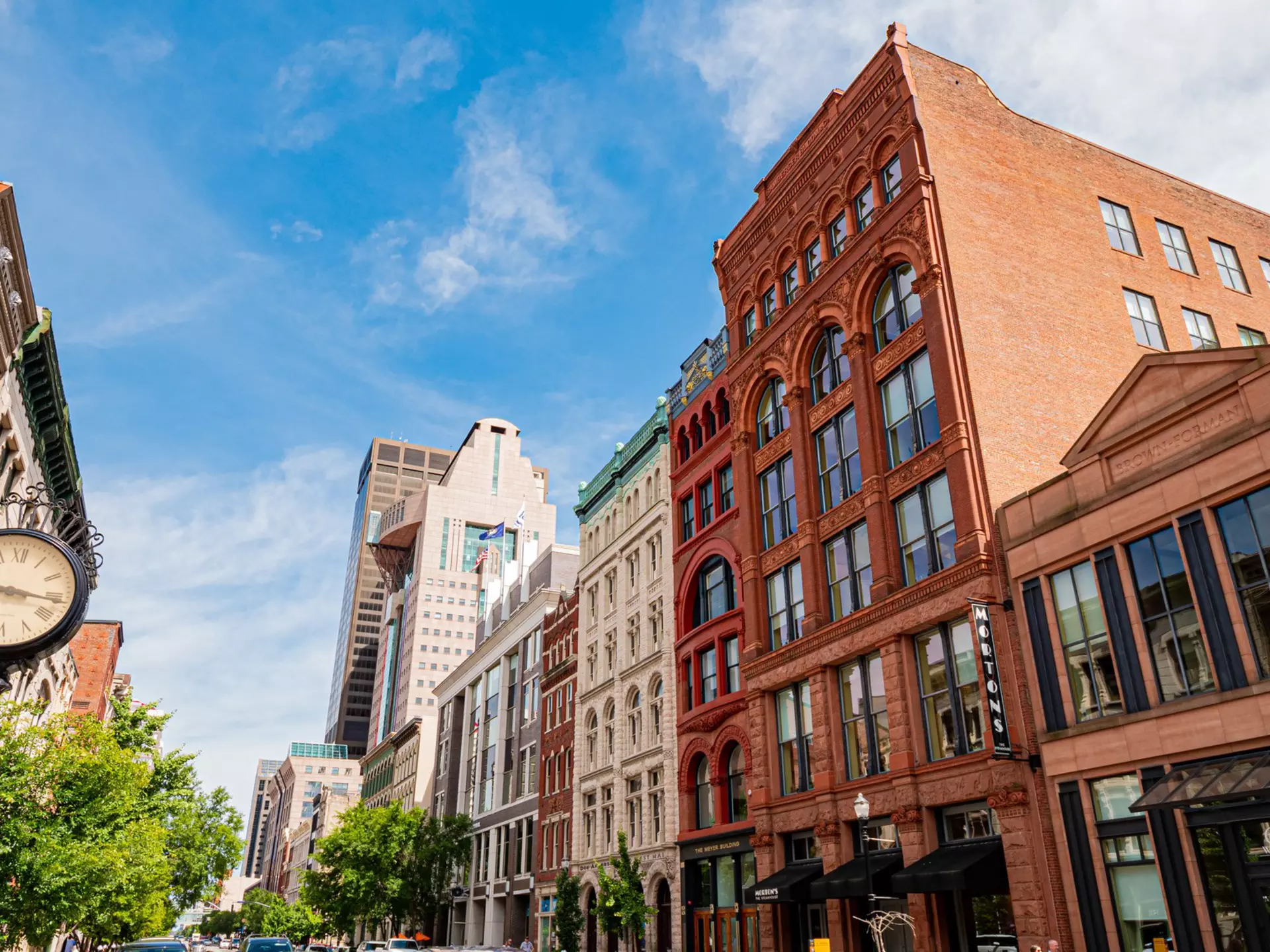 Street view of Louisville, Kentucky, with buildings on both sides and clock on a street post in the foreground.