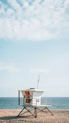 White lifeguard stand with orange signs on it on a beach with the ocean in the background