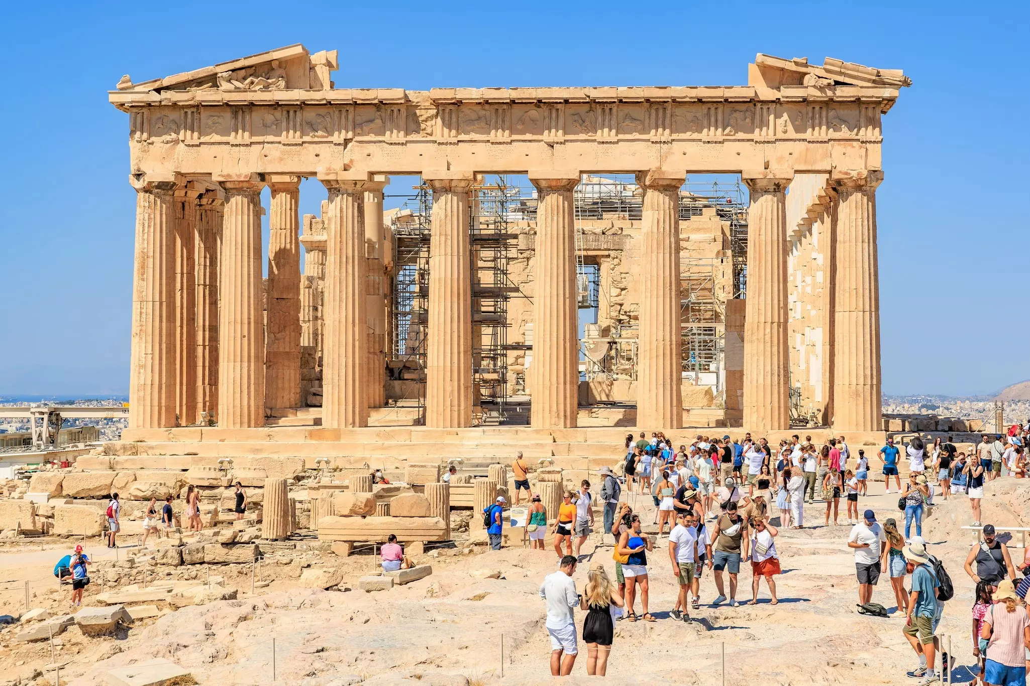 A large group of people are gathered near the ruins of a building with large columns