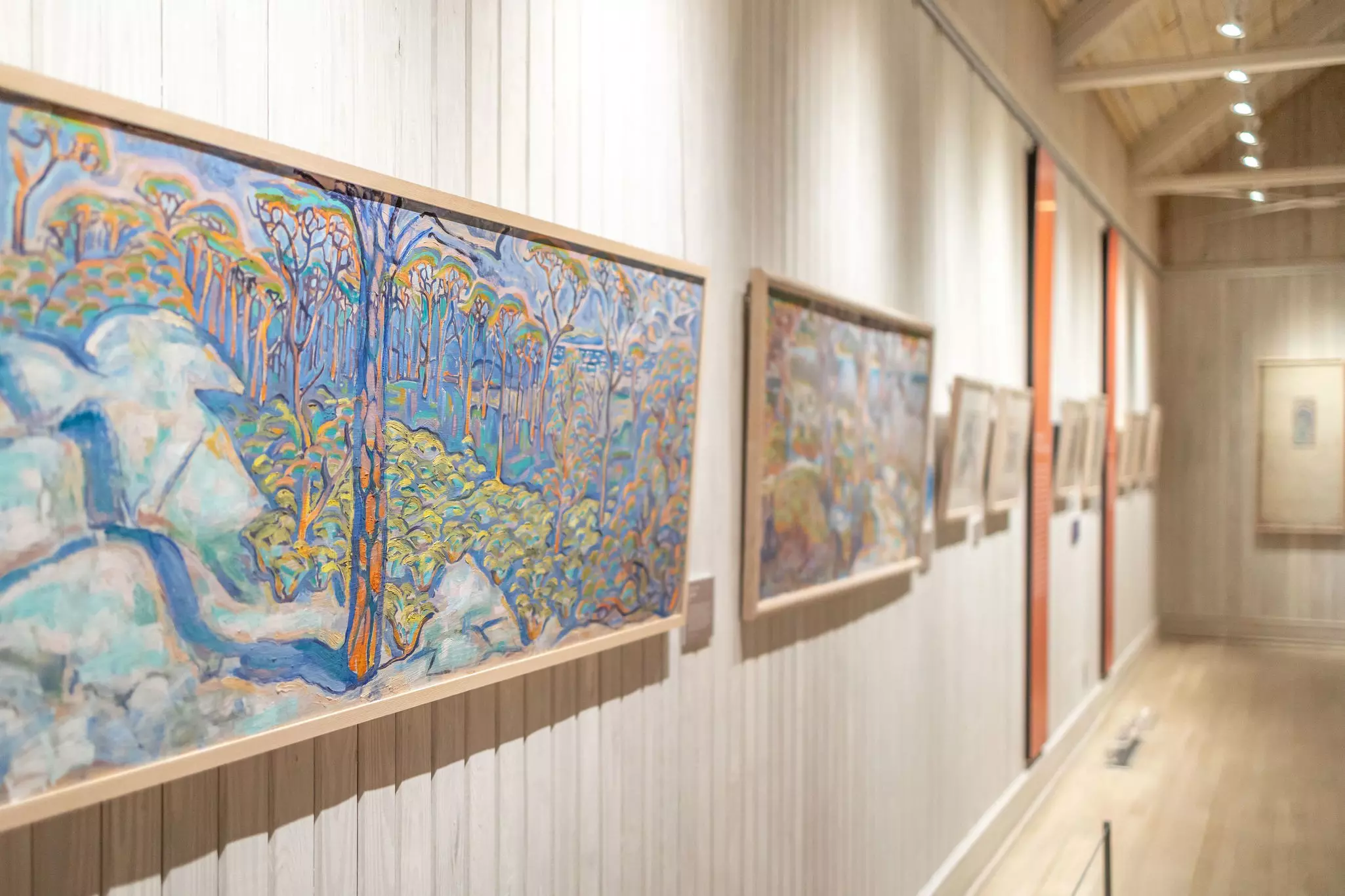 Paintings in soft colors hang on the wall of museum gallery.