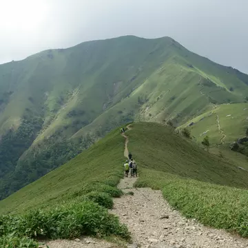 A wide-angle shot of people walking a grass-lined trail on Mount Tsurugi